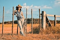 A cowgirl leaning on a fence. Descriptive picture of Tailor Hill Stations song "To The Beat Of Your Heart".